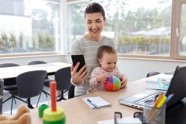 Мати з дитиною і телефоном працює в домашньому офісі — стокове фото