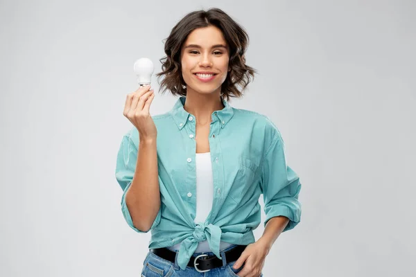 Улыбающаяся женщина держит энергосберегающую лампочку — стоковое фото