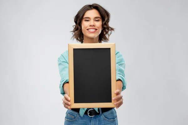 Portrét usmívající se ženy ukazující černou tabuli — Stock fotografie