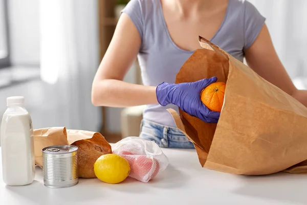 Vrouw in handschoenen het nemen van voedsel uit papieren zak thuis — Stockfoto
