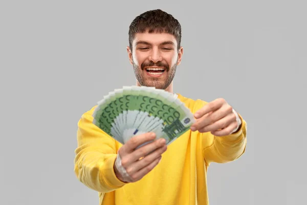 Smiling young man in yellow sweatshirt with money — Stock Photo, Image