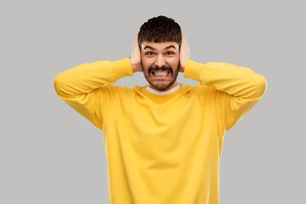 Hombre en sudadera amarilla cerrando orejas por las manos — Foto de Stock