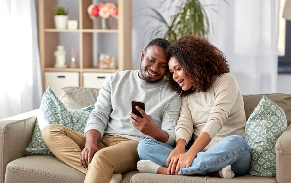 Szczęśliwa para ze smartfonem i słuchawkami w domu — Zdjęcie stockowe