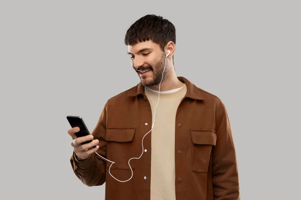 Улыбающийся молодой человек с наушниками и смартфоном — стоковое фото