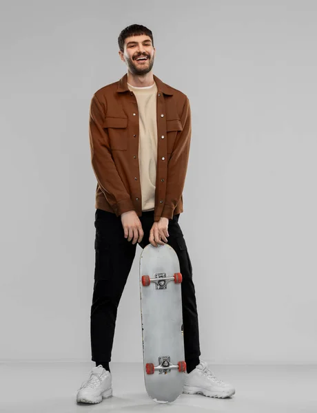 Smiling young man in brown jacket with skateboard — Stock Photo, Image