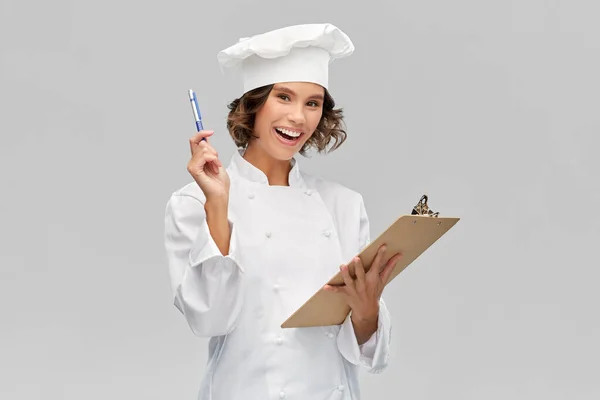 Glimlachende vrouwelijke chef in toque met klembord — Stockfoto