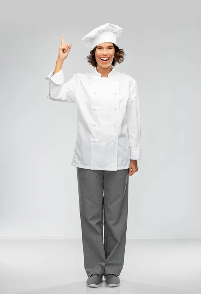 Glimlachende vrouwelijke chef-kok in toque wijzende vinger omhoog — Stockfoto