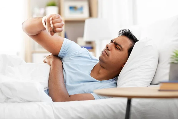 Indian man in bed looking at smart watch at home — Stok fotoğraf