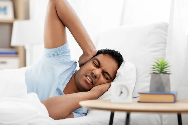 Annoyed indian man with alarm clock lying in bed — Φωτογραφία Αρχείου
