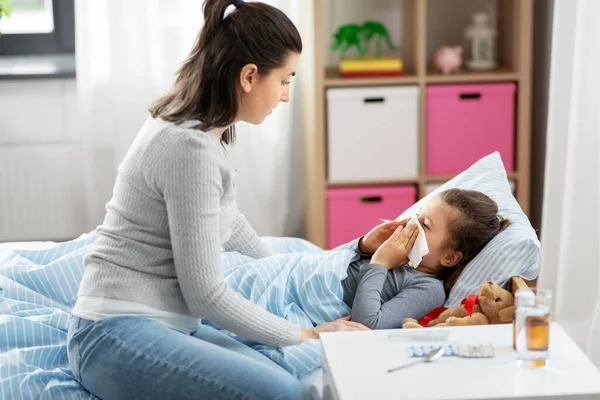 Mãe e filha pequena doente soprando nariz na cama — Fotografia de Stock