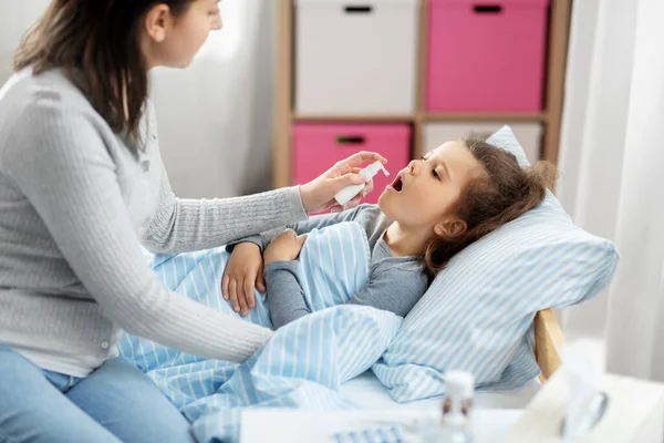 Mother with oral spray treats sick little daughter — Stock Photo, Image