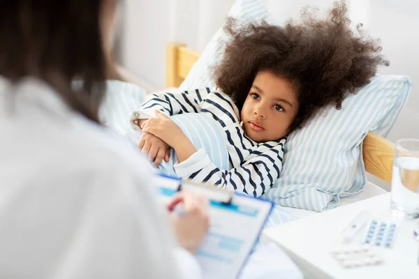 Doctor with clipboard and sick girl in bed at home — Stock Photo, Image