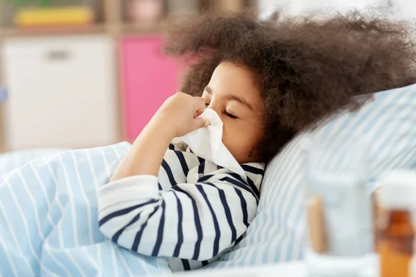 Chica enferma acostada en la cama y sonándose la nariz en casa —  Fotos de Stock