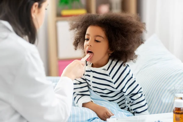 Doctor checking sick girls throat at home — Stock Photo, Image