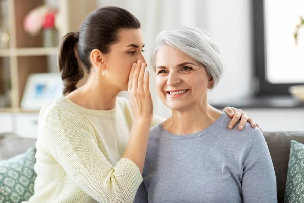 adult daughter whispering secret to senior mother