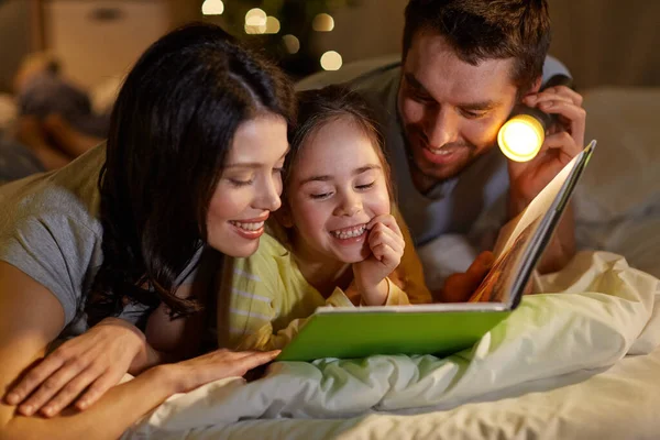 Happy family reading book in bed at night at home — Stock Photo, Image