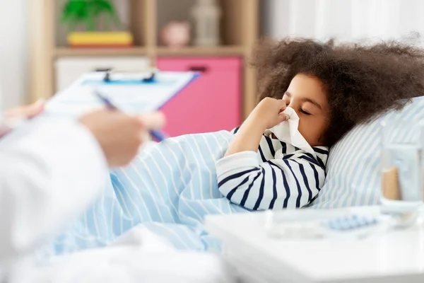 Lékař a nemocná dívka v posteli foukání nos — Stock fotografie