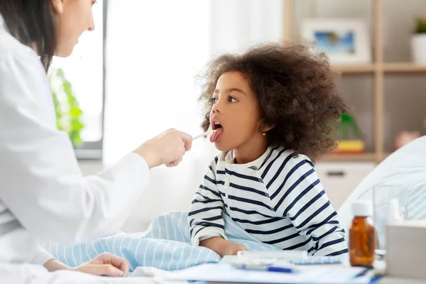 Doctor checking sick girls throat at home — Stock Photo, Image