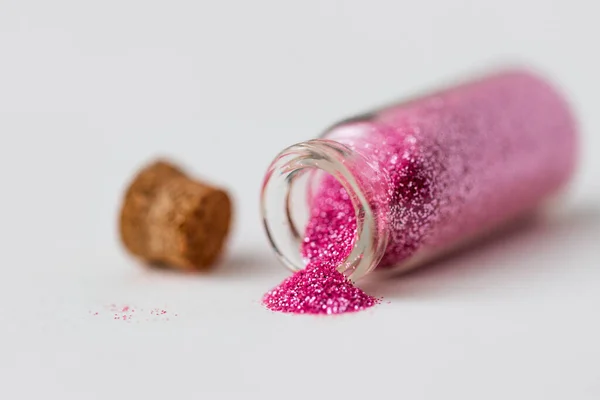Glitters rosa derramado a partir de pequena garrafa de vidro — Fotografia de Stock