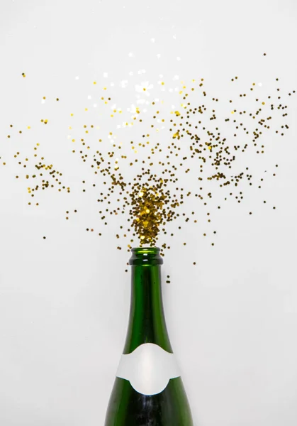 Champagne bottle and golden glitters on white — Stock Photo, Image