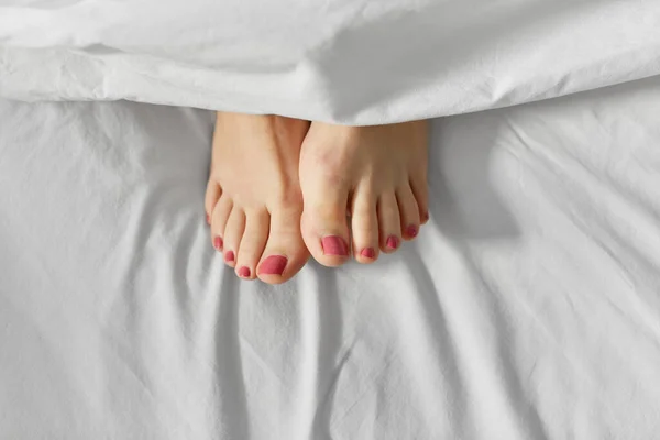 Pies de mujer acostada en la cama debajo de una manta blanca —  Fotos de Stock
