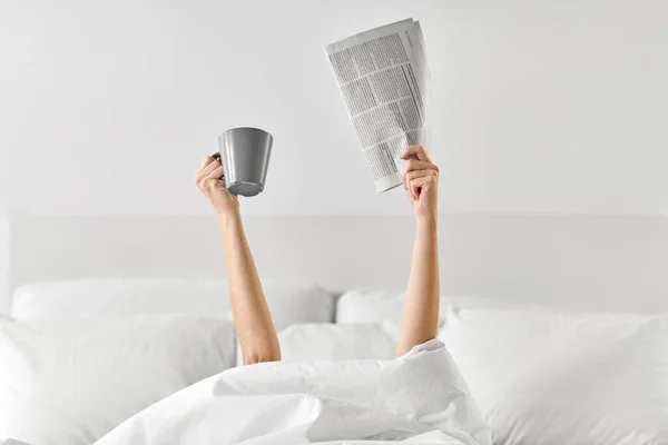 Frau mit Kaffee und Zeitung im Bett liegend — Stockfoto