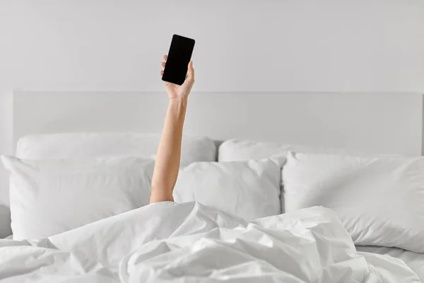 Рука женщины лежит в постели со смартфоном — стоковое фото