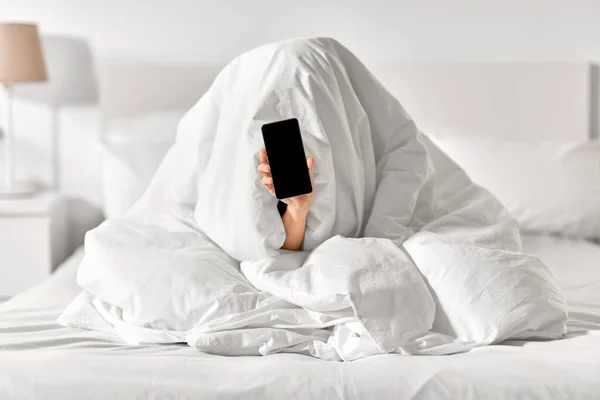 Mujer con teléfono sentado debajo de la manta en la cama —  Fotos de Stock