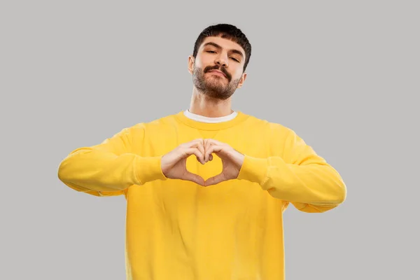 Young man in yellow sweatshirt I making hand heart — стоковое фото