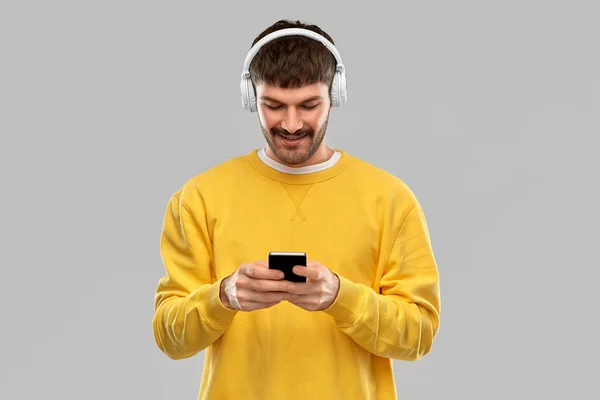 Usmívající se mladý muž se sluchátky a smartphonem — Stock fotografie
