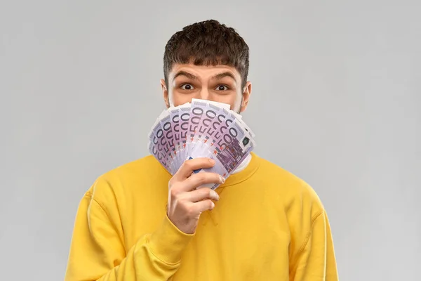 Happy young man in yellow sweatshirt with money — Stockfoto