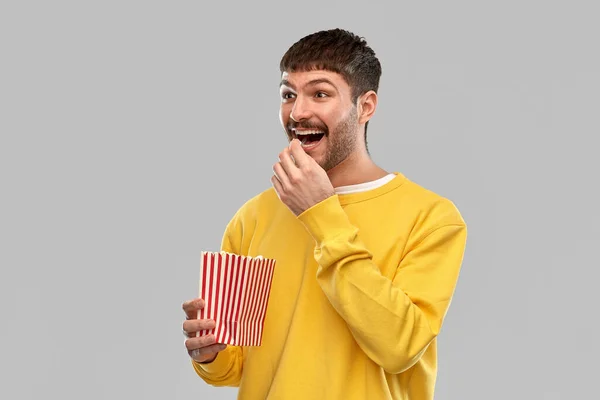 Smiling man in yellow sweatshirt eating popcorn — ストック写真