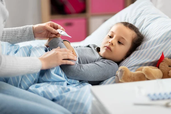 mother measuring temperature of sick daughter