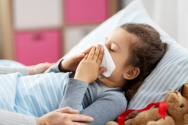 Mother and ill little daughter blowing nose in bed — Stock Photo, Image