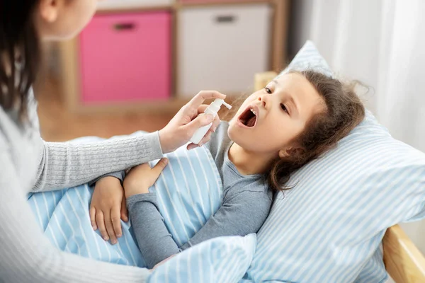 Mother with oral spray treats sick little daughter — Stock Photo, Image