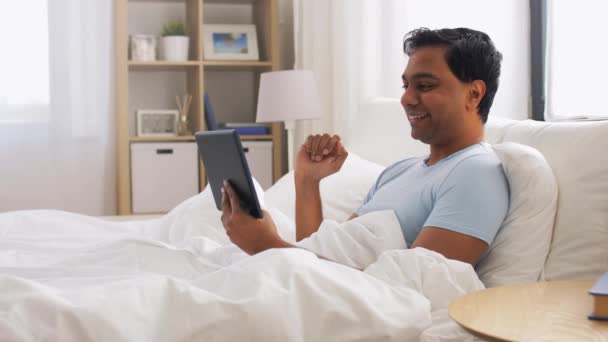Happy indian man with tablet pc in bed at home — Stock Video