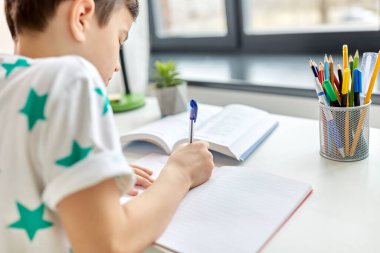 close up of boy writing to notebook at home clipart