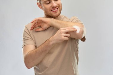 young man applying pain medication to his elbow clipart