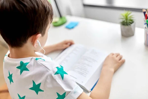 Menino com fones de ouvido e livro didático de aprendizagem em casa — Fotografia de Stock