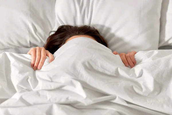 Woman lying in bed under white blanket or duvet — Stock Photo, Image