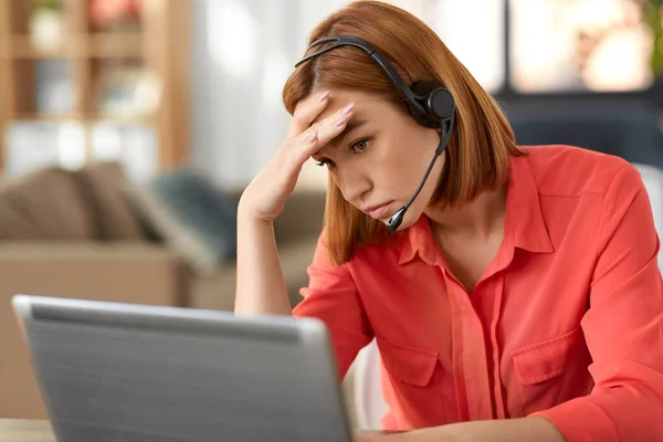 Ledsen kvinna med headset och bärbar dator arbetar hemma — Stockfoto