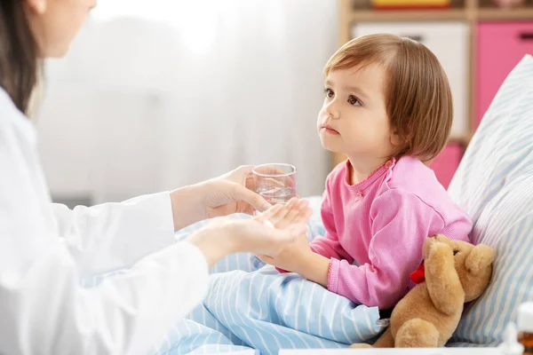 Médico dando medicamentos a la niña enferma en la cama en casa —  Fotos de Stock