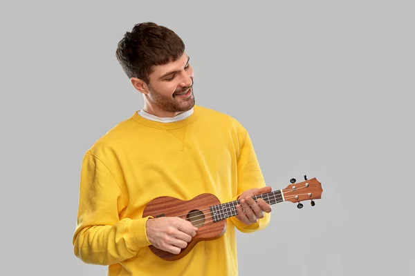 Uśmiechnięty młody człowiek gra na gitarze ukulele — Zdjęcie stockowe