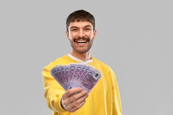 Lächelnder junger Mann im gelben Sweatshirt mit Geld — Stockfoto