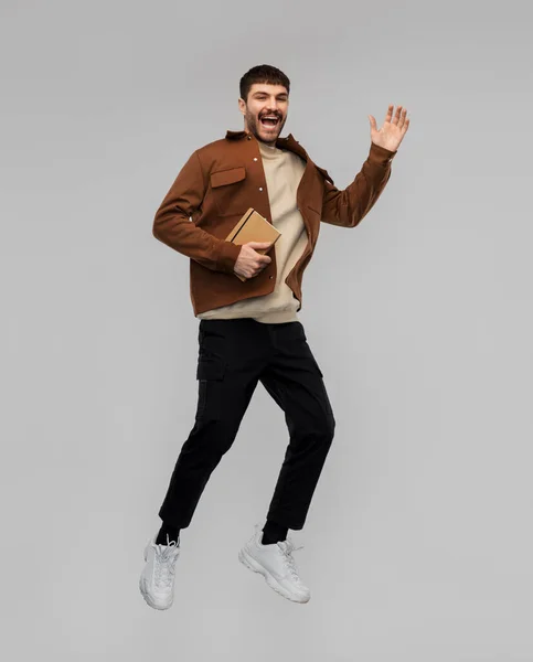 Счастливый улыбающийся молодой человек с дневником прыгая в воздух — стоковое фото