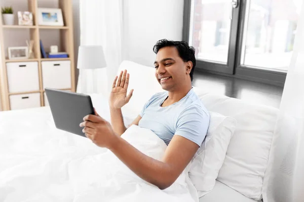 Hombre feliz con la tableta PC en la cama teniendo videollamada —  Fotos de Stock