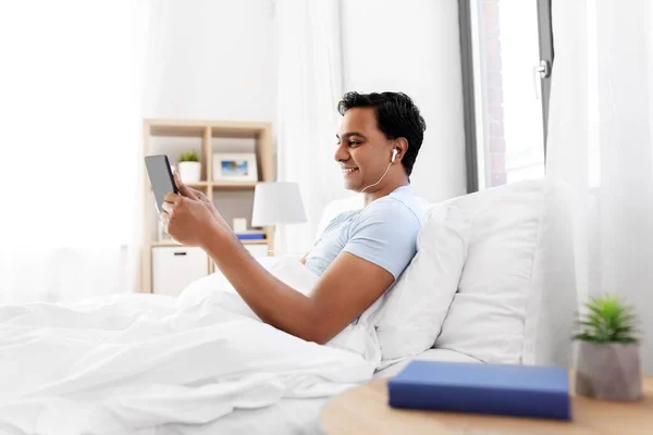 Hombre indio feliz con la tableta PC en la cama en casa —  Fotos de Stock