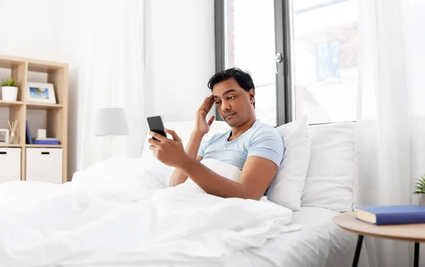 Hombre indio soñoliento en la cama mirando el teléfono inteligente —  Fotos de Stock
