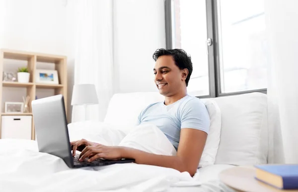 Glücklicher indischer Mann mit Laptop im Bett zu Hause — Stockfoto