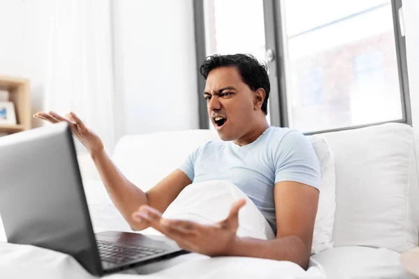 Rozzlobený indián s laptopem v posteli doma — Stock fotografie